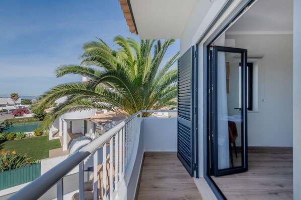 A balcony with a view of a pool and palm trees, a sliding glass door, and a wooden floor.