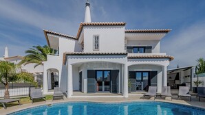 Une maison moderne à deux étages avec piscine, dotée d’une façade blanche, d’un toit en tuiles et de nombreuses fenêtres.