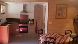 Cocina compacta con estufa, horno y lavamanos. Hay una mesa de comedor con sillas y un tapete rojo.