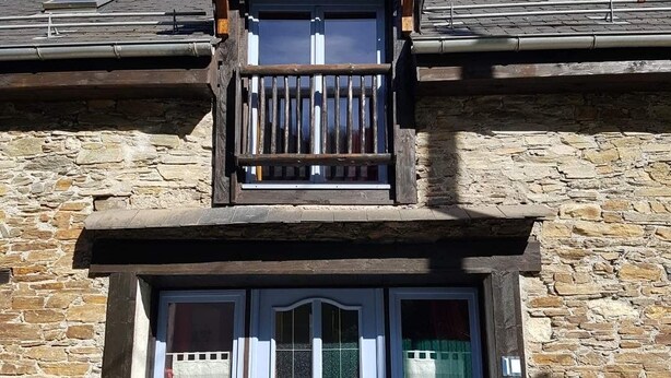 Un edificio de piedra con un balcón de madera, una puerta doble y un ventanal pequeño.
