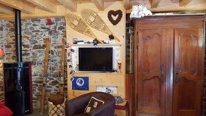Una sala de estar acogedora con pared de piedra, vigas de madera, chimenea, esquíes, televisor y un mueble de madera grande.