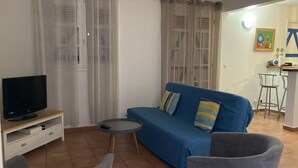 A living room with a blue sofa, two grey armchairs, a small round table, a TV on a wooden stand, and a kitchen area in the background. - COMFORTABLE VILLA WITH PRIVATE POOL  (SAINT FRANCOIS)