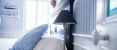 A bedroom with a bed, a lamp, and a window with striped curtains.