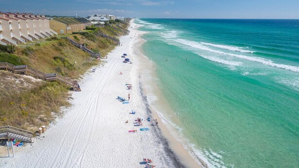 Una playa con una hilera de edificios a lo largo de la orilla, arena y el océano.