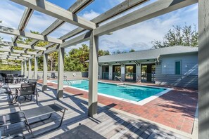 Un espacio exterior techado con piscina, mobiliario de patio y un edificio al fondo.