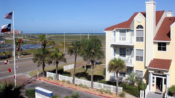 A beachfront hotel with a white fence, palm trees, and a clear view of the ocean. - Beach Views and Cozy (Corpus Christi)