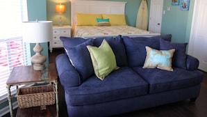 A bedroom with a bed, a blue sofa, a nightstand with a lamp, and a surfboard. - Beach Views and Cozy (Corpus Christi)