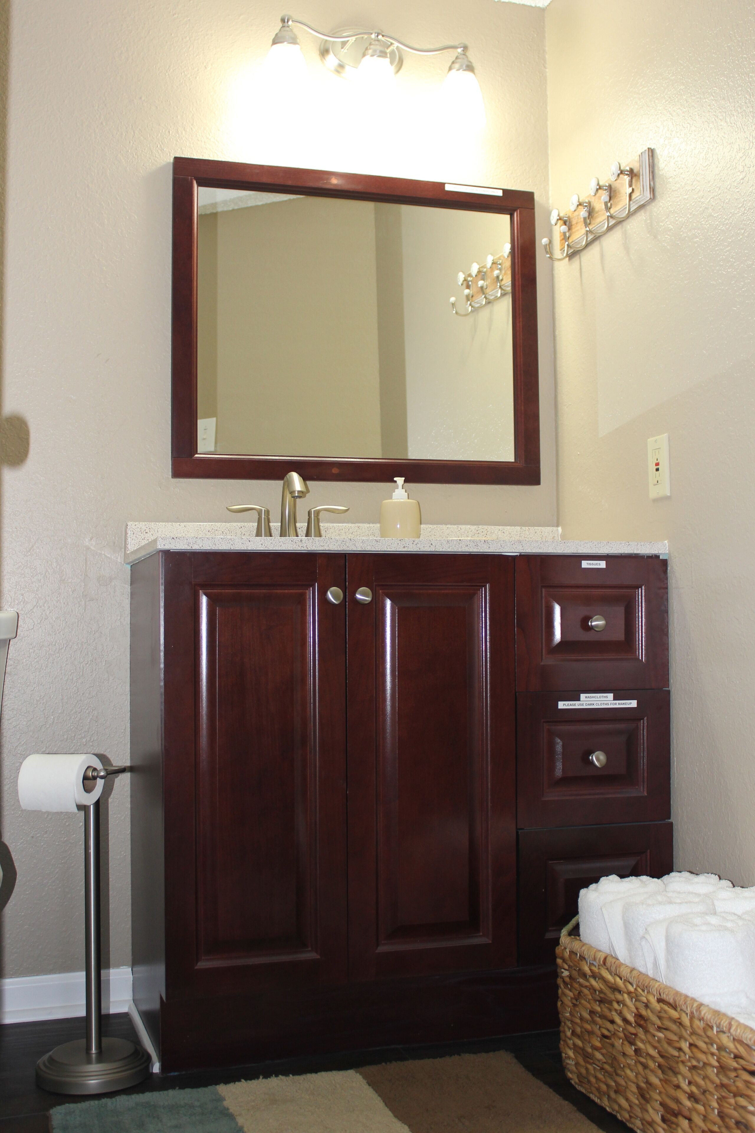 A bathroom with a wooden vanity, a mirror, a towel rack, and a basket of towels.