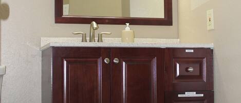 A bathroom with a wooden vanity, a mirror, a towel rack, and a basket of towels.