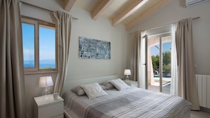 Un dormitorio con cama, mesitas de noche, una ventana con cortinas, un cuadro en la pared y vistas a través de la ventana.