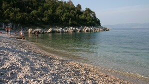 Una playa de guijarros con gente cerca del agua, rodeada de árboles y acantilados rocosos.