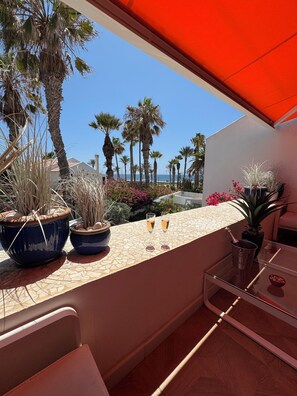 A balcony with potted plants, two glasses of champagne, and a view of the beach and palm trees. - Location, location, location (Arona)