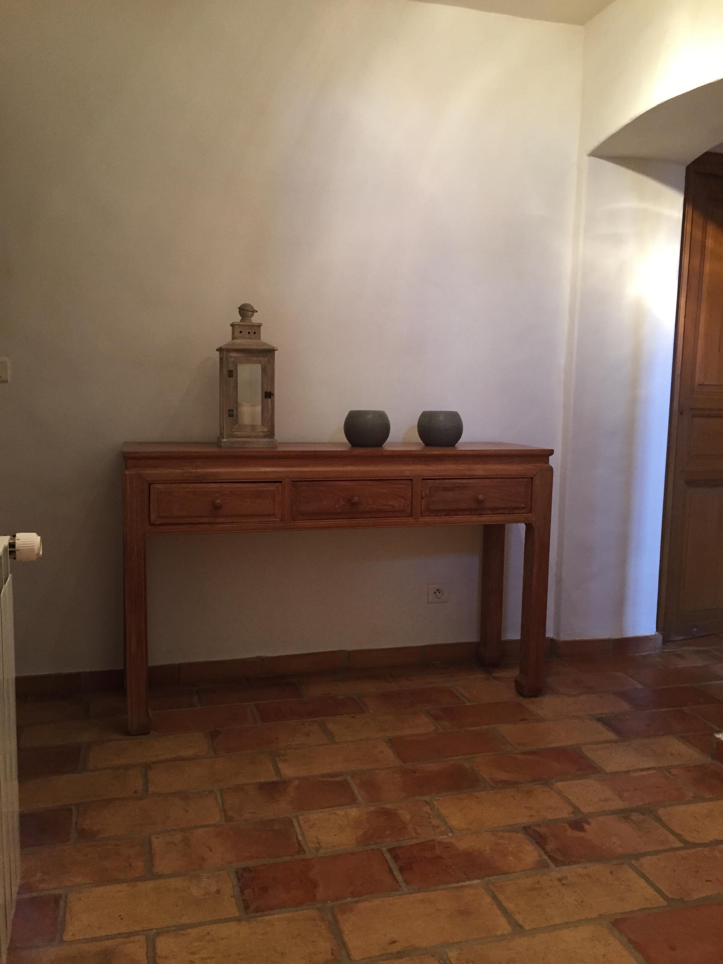 A wooden console table with two ceramic bowls and a lantern, set against a plain wall with a tiled floor.