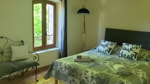 A bedroom with a bed, a bench, a floor lamp, and a window with curtains.