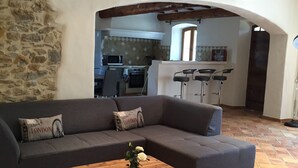 A living room with a dark grey sectional sofa, a wooden coffee table with a vase of white flowers, and a stone wall.