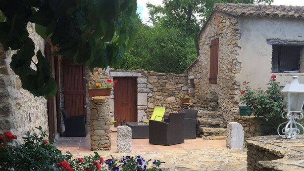 A stone courtyard with a rustic stone wall, a wooden door, and a seating area with a table and chairs.