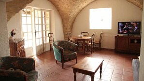 Une pièce rustique avec un plafond voûté, une table à manger en bois, des chaises, un téléviseur et une fenêtre laissant entrer la lumière naturelle.