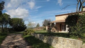 Une propriété aux murs de pierre, dotée d’un toit en tuiles, d’une allée pavée et d’un espace verdoyant avec des arbres.