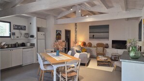 A modern kitchen with white cabinetry, a dining table with chairs, a sofa, a television, and a vase with flowers. - House sea view in Chaucre beach 80 m panoramic solarium  (Saint-Georges-D'oléron)