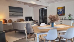 A modern living room with a sofa, a dining table with chairs, a TV, and artwork on the walls. - House sea view in Chaucre beach 80 m panoramic solarium  (Saint-Georges-D'oléron)
