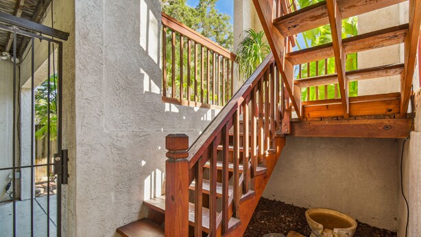 Una escalera de madera con una puerta de metal en la base, que lleva a un balcón con vistas a zonas verdes.