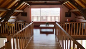 Una escalera de madera que conduce a un balcón con baranda de madera, una mesa con flores y una ventana con persianas.