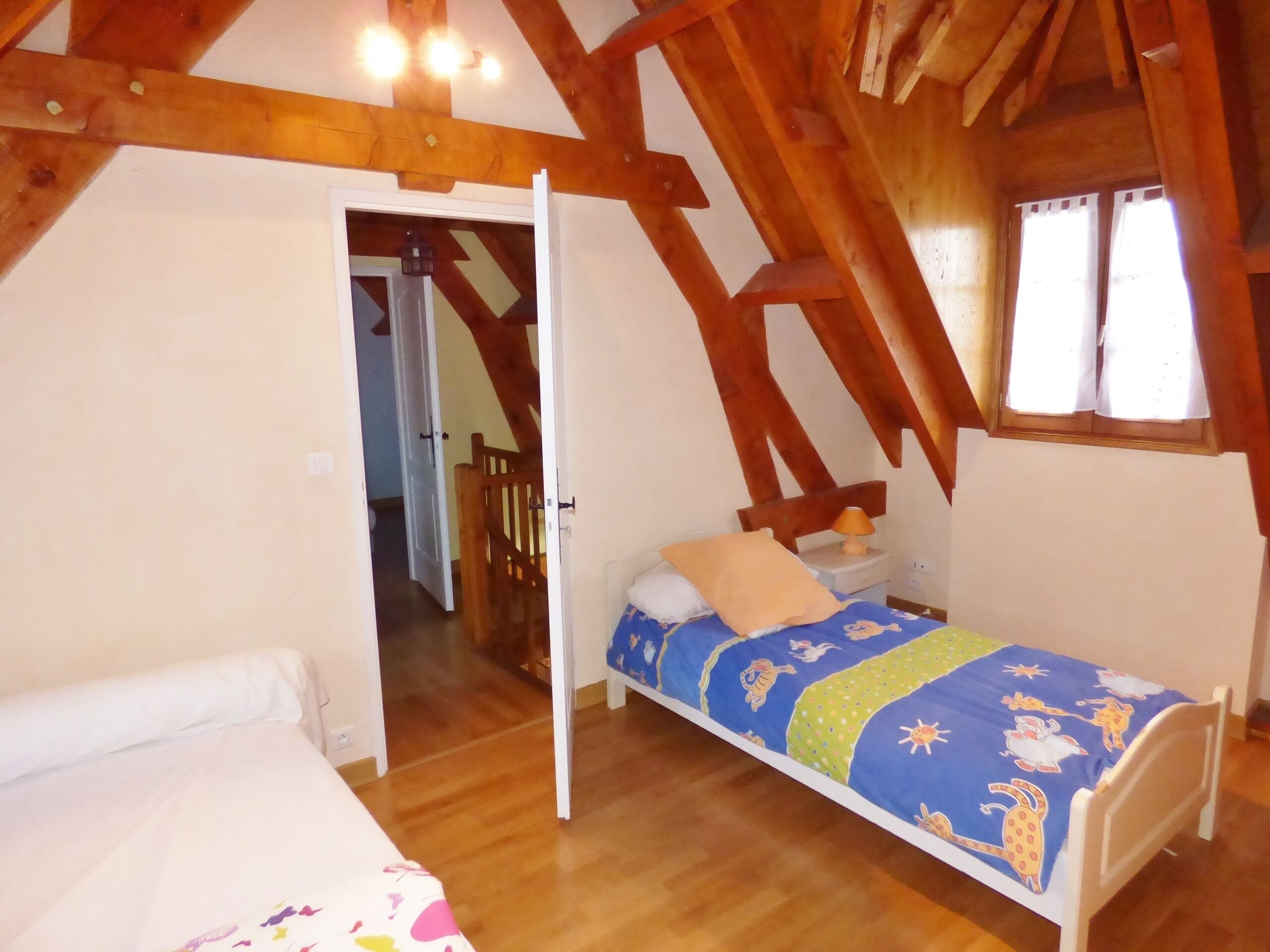 A bedroom with a wooden ceiling, a single bed with a colorful bedspread, a nightstand with a lamp, and a window with curtains.