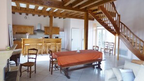 Una cocina amplia con vigas de madera, un comedor con mesa y sillas, y una escalera que conduce a un nivel superior.