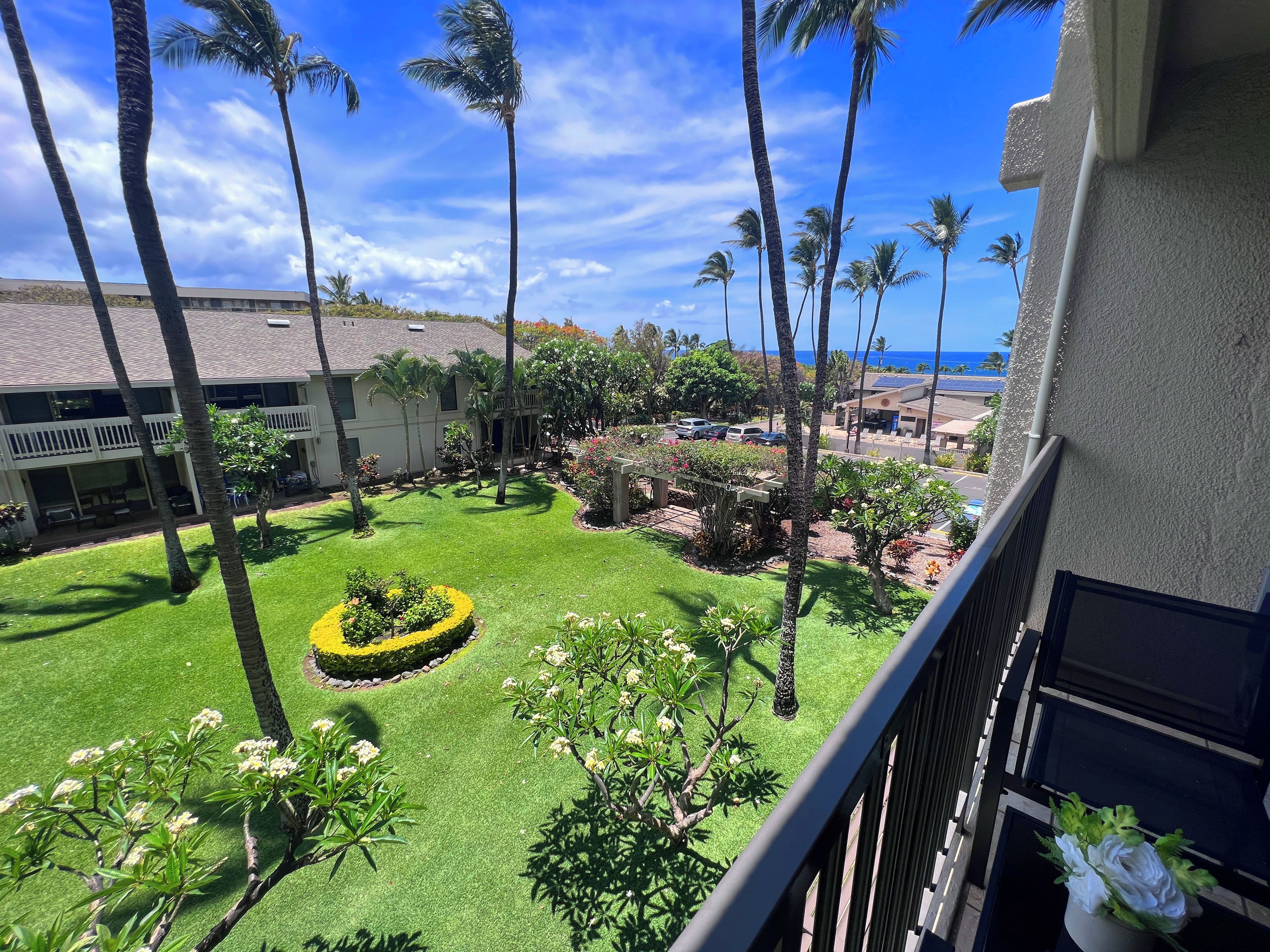 A well-maintained courtyard with palm trees, a neatly trimmed lawn, and a view of the ocean.
