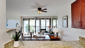 A kitchen with granite countertops, wooden cabinets, a ceiling fan, and a dining area with a table and chairs. - Breezy Kihei Condo Ocean and Haleakala Views Lanai Across From Kamaole (Kihei)