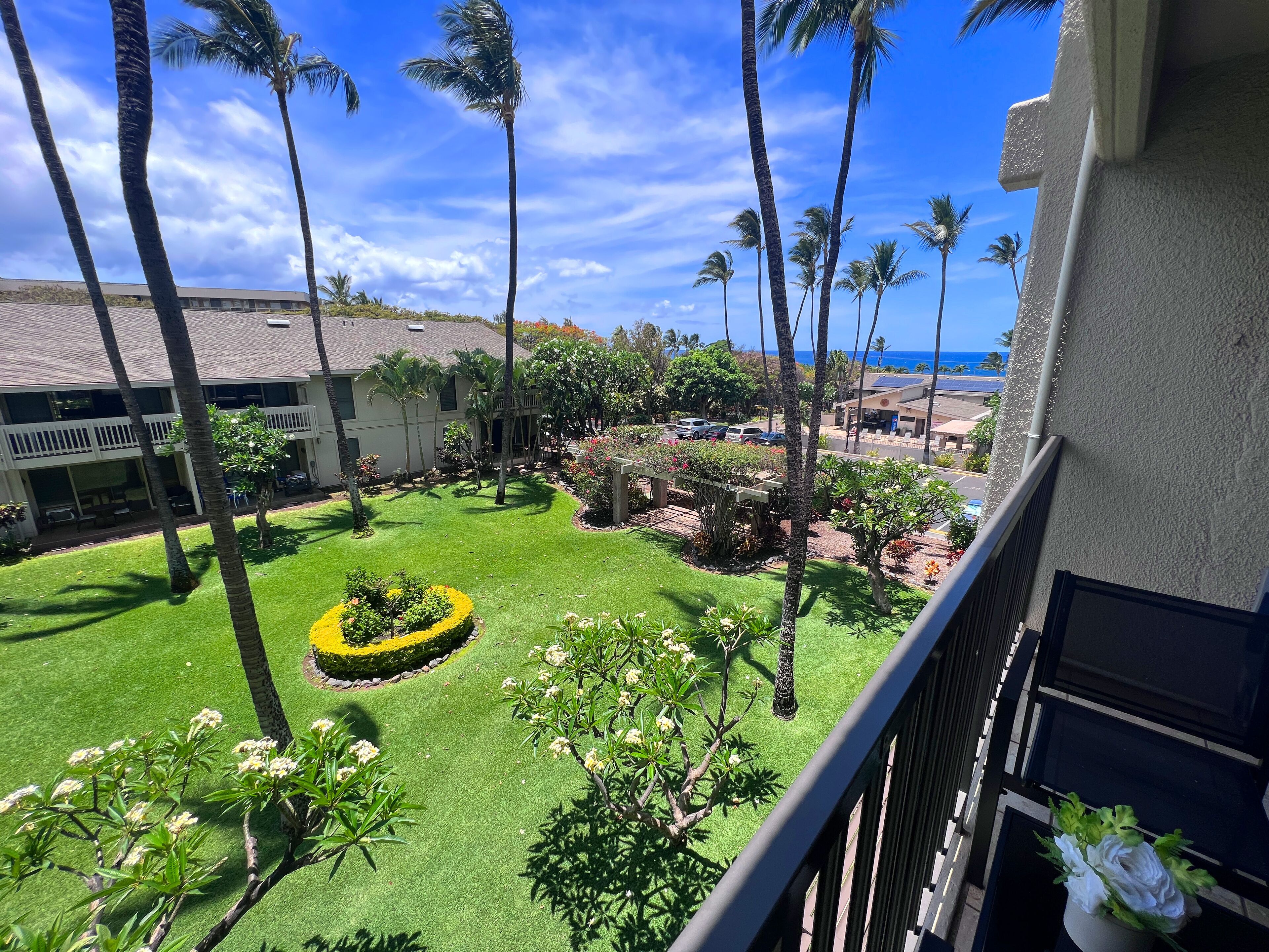 A well-maintained courtyard with palm trees, a neatly trimmed lawn, and a view of the ocean.
