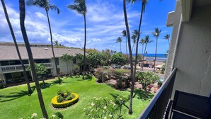 A well-maintained courtyard with palm trees, a neatly trimmed lawn, and a view of the ocean. - Breezy Kihei Condo Ocean and Haleakala Views Lanai Across From Kamaole (Kihei)