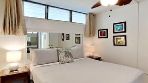 A neatly arranged bedroom with a large bed, bedside lamps, a wooden nightstand, a mirror, and framed pictures on the wall. - Breezy Kihei Condo Ocean and Haleakala Views Lanai Across From Kamaole (Kihei)