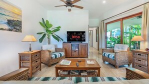 A living room with wicker furniture, a flat-screen TV, a ceiling fan, and a large plant. - Villa #3 - Isla Retreats | Tropical Gardens + Pool (Isla Mujeres)