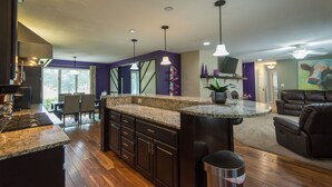 A modern kitchen with dark cabinets, granite countertops, and pendant lighting. - LUXURY GETAWAY! ARCADE, POOL TBL, PING PONG, HOT TUB, DECK! ACCESS TO POOLS! (Waukee)