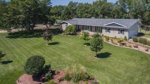 A two-story house with a stone facade, a large front lawn, and a driveway. - LUXURY GETAWAY! ARCADE, POOL TBL, PING PONG, HOT TUB, DECK! ACCESS TO POOLS! (Waukee)