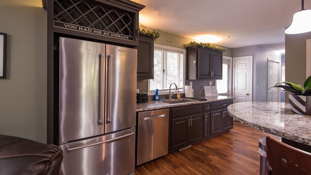 A modern kitchen with stainless steel appliances, dark cabinetry, and a granite countertop. - LUXURY GETAWAY! ARCADE, POOL TBL, PING PONG, HOT TUB, DECK! ACCESS TO POOLS! (Waukee)