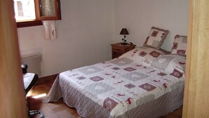 Ein Schlafzimmer mit einem Bett, einem Nachttisch, einer Lampe und einem Fenster mit Vorhängen.