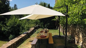 Un espacio de comedor al aire libre con mesa, bancos, un gran paraguas y un muro de piedra.