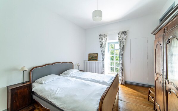 A bedroom with a bed, a nightstand, a dresser, a radiator, and a window with curtains. - PROMOTION - Luxury 16th century Chateau - private river - 25 pax (Scey-Maisières)