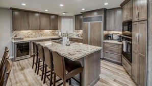 Une cuisine moderne avec des meubles en bois foncé, un plan de travail en marbre, des appareils électroménagers en acier inoxydable et un îlot central doté de tabourets de bar.