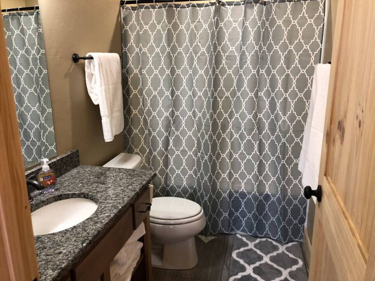 Een badkamer met een douchegordijn met patroon, een wit toilet, een wastafel met granieten blad en een spiegel.