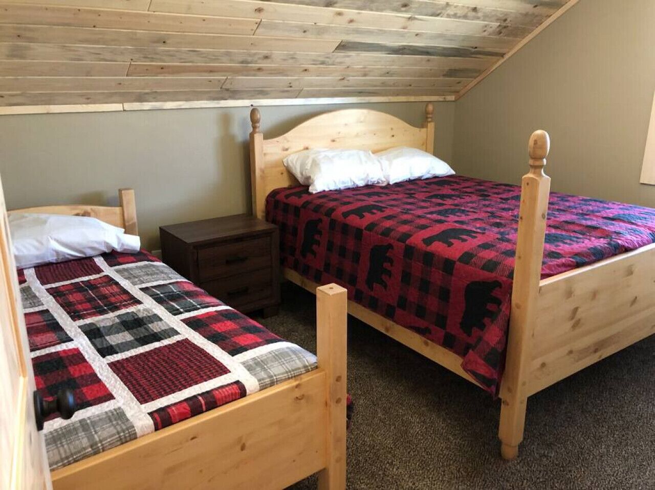 A bedroom with two wooden beds, each with a quilted bedspread. There is a wooden nightstand between the beds.