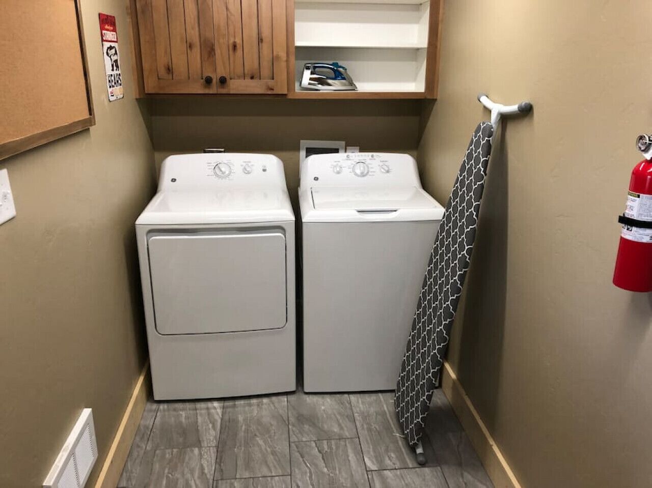 A laundry room with two stacked washers and dryers, a fire extinguisher, and a towel rack.