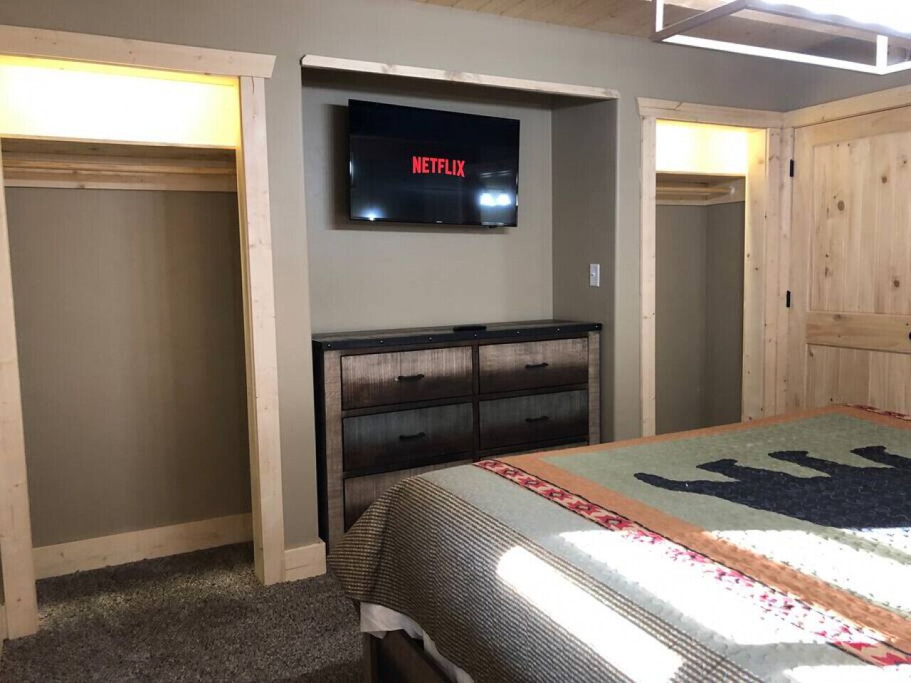Un dormitorio con una cama, un televisor montado en la pared y un armario de madera.