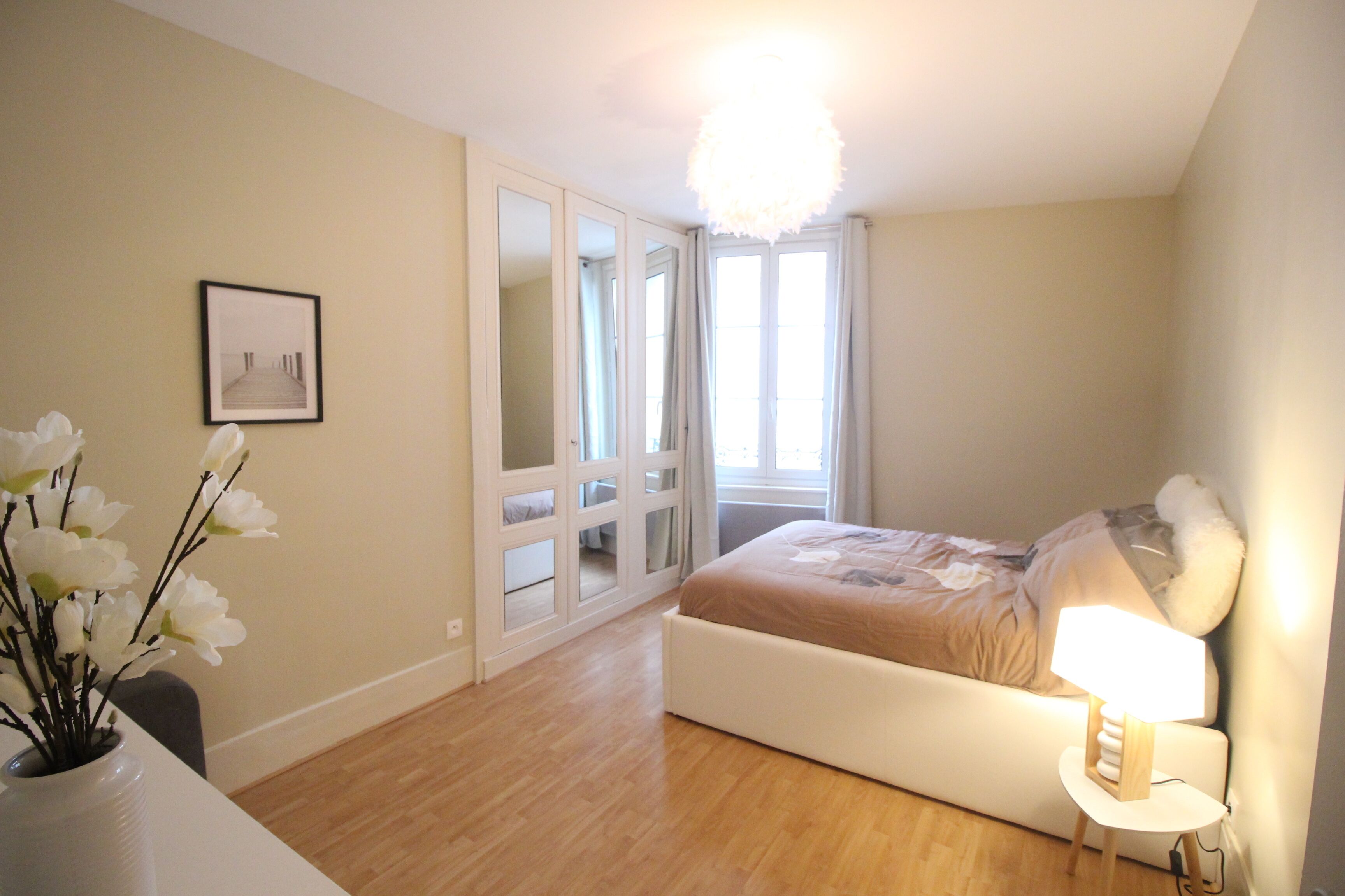 Een slaapkamer met een bed, een bedlampje en een vaas met bloemen.