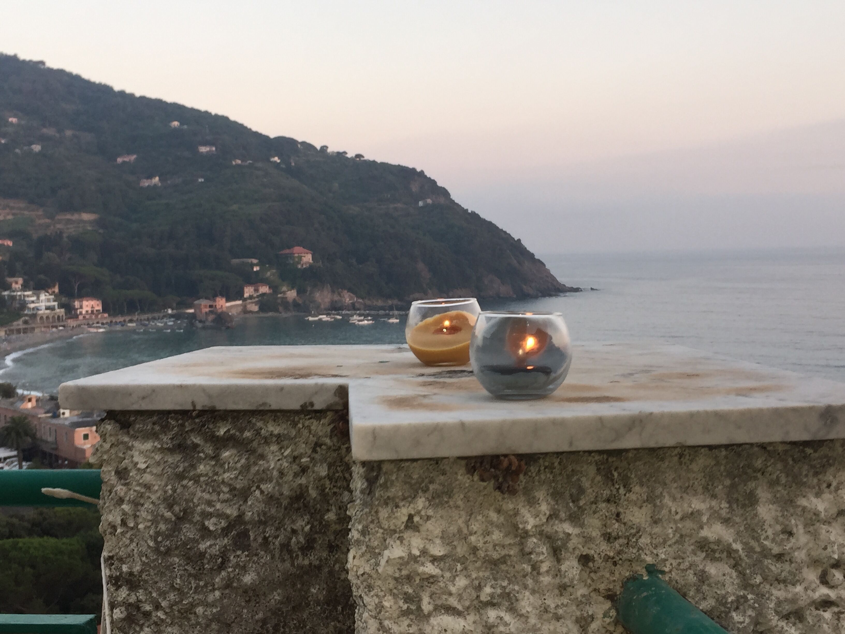 Une vue sur la mer avec une corniche en pierre, deux bougies et une côte lointaine.