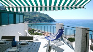 A terrace with a view of the sea, a table set with plates and cutlery, and a blue chair.