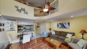 A spacious living area with a kitchen, a dining table with chairs, a sofa, and a coffee table. - Where Families Gather Kihei 2BR Loft Condo Heated Pool Hot Tub Near Beach (Kihei)