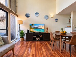 Un salon moderne avec un plancher en bois, un téléviseur à écran plat, un coin repas avec des chaises et un mur décoré d’assiettes.
